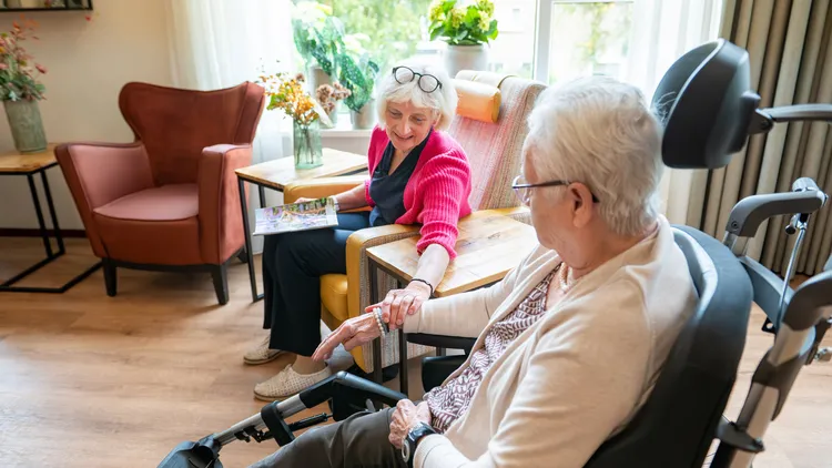 Oudere dame op bezoek bij bewoner in rolstoel - foto Niels Zomer