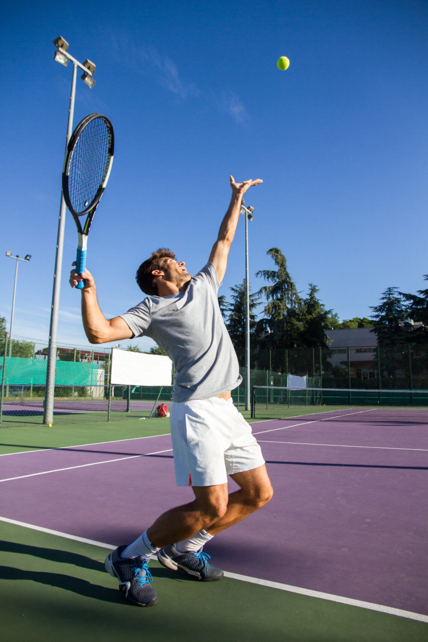 Professional tennis player is doing a kick tennis on a tennis court on a sunny summer morning. The is dressed in sportswear.